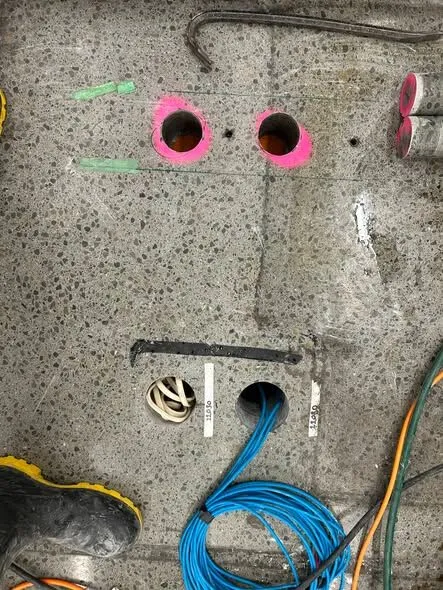 Blue data cable pulled up through a cored hole in a South Canterbury supermarket floor, with labelled duct markers on the slab