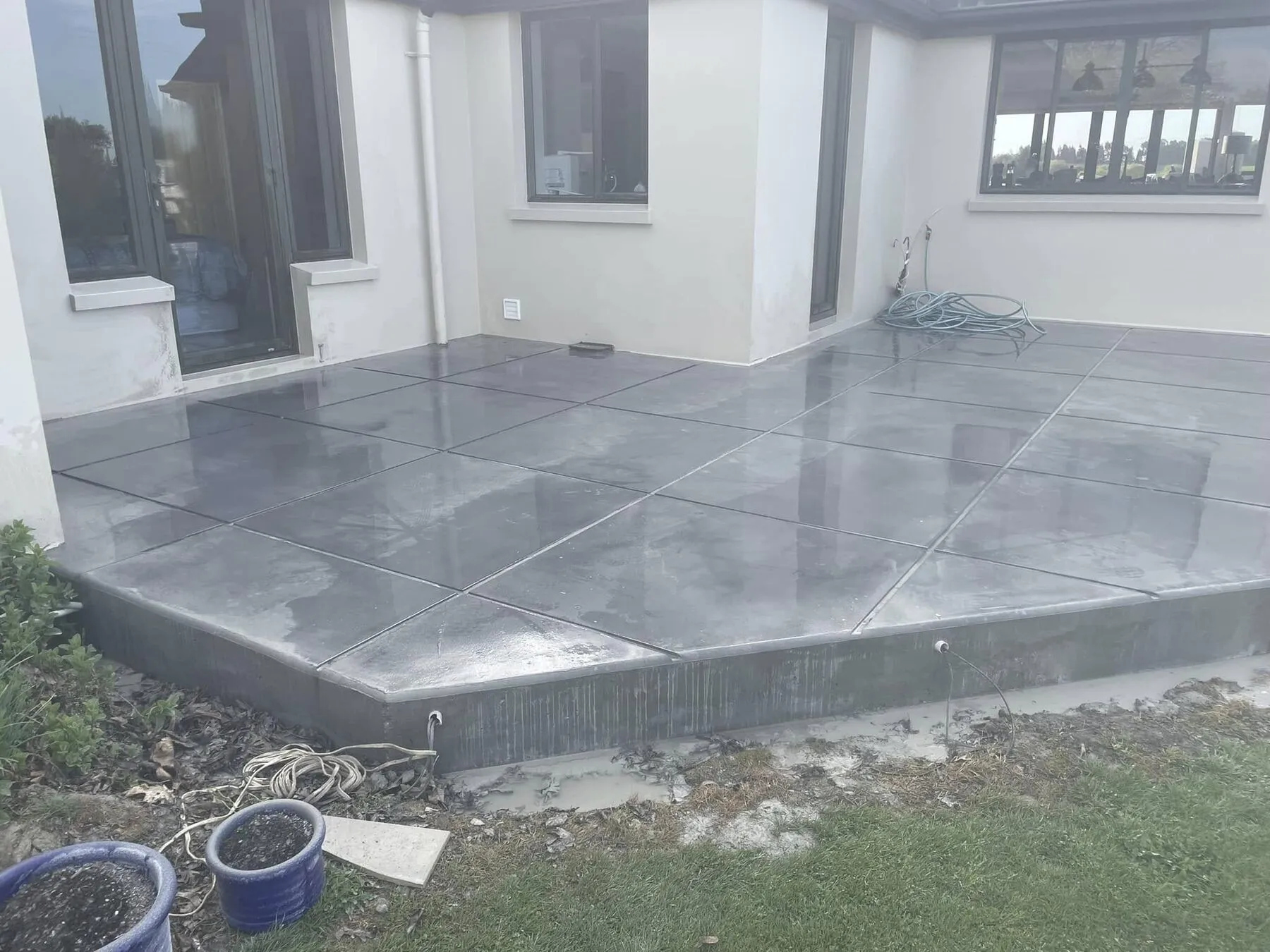 Finished patio beside a house near Timaru, cut into large squares with wide decorative saw cuts, lawn and garden at the edge