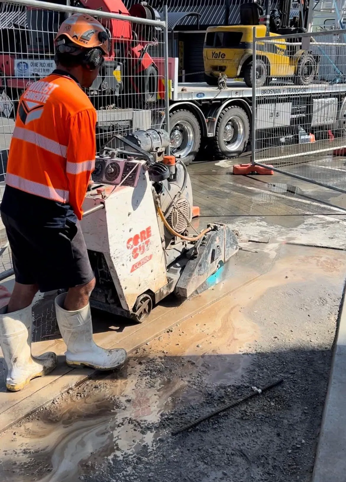 Direct Concrete operator running a road saw on a fenced commercial site in Timaru, truck and cones behind