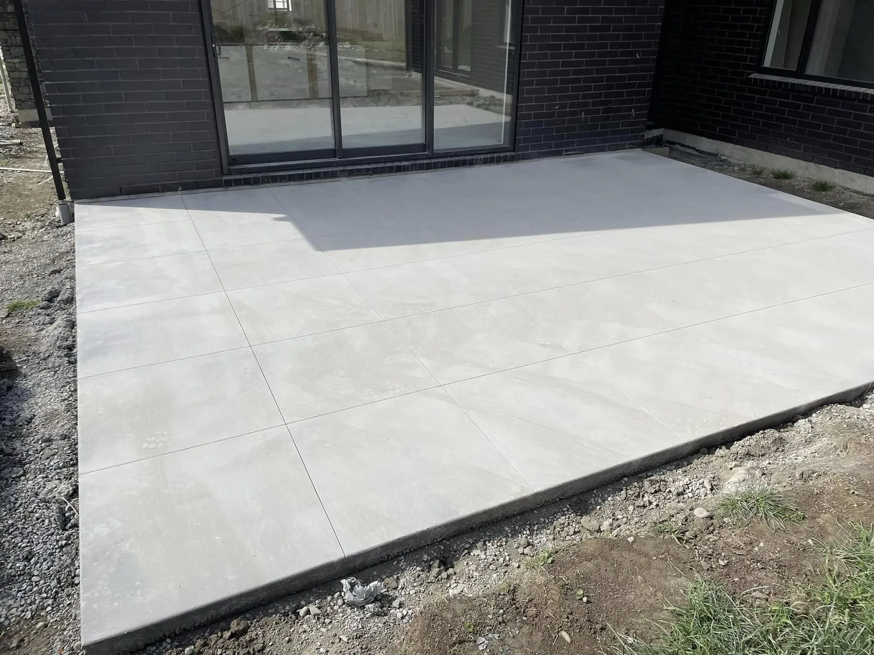 Corner of a South Canterbury concrete patio showing wide 20 mm decorative saw cuts running to the edge
