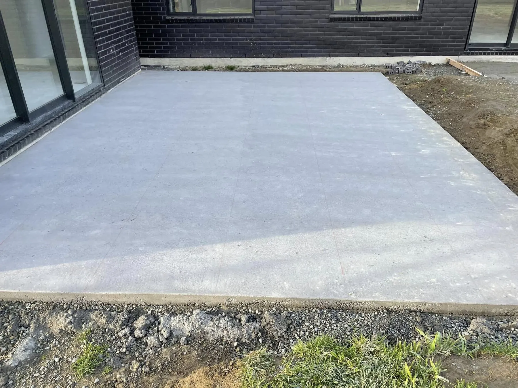 Newly poured plain concrete patio outside a dark brick house, before any cutting