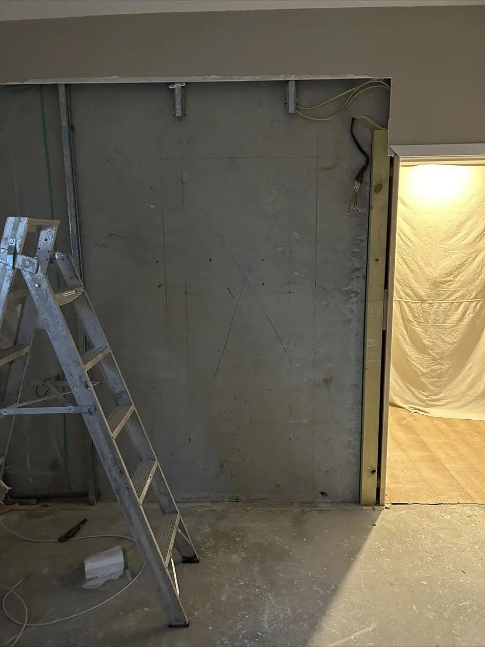 New doorway opening marked out in pencil on an interior concrete wall in South Canterbury, ladder alongside and the room beyond sheeted off